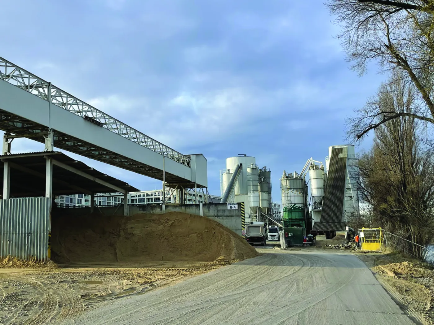 Současný stav areálu betonárny – mostní dopravník štěrku, halda kameniva a zásobníky za nezpevněnou cestou